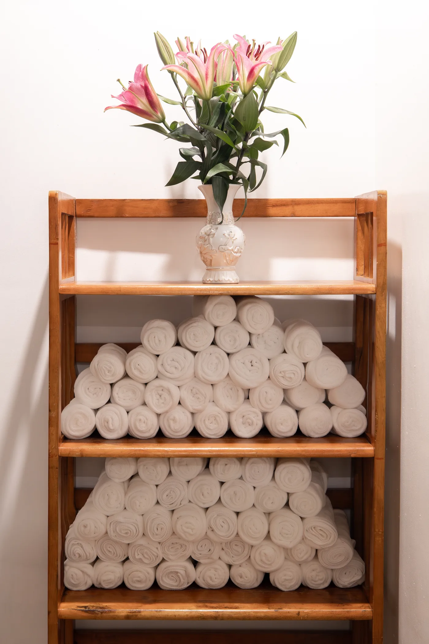 Fresh rolled towels and flowers on a wooden shelf